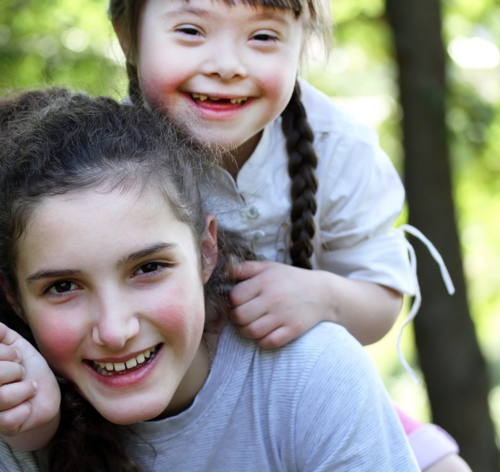 young girl with down syndrome laughing and embracing with friend